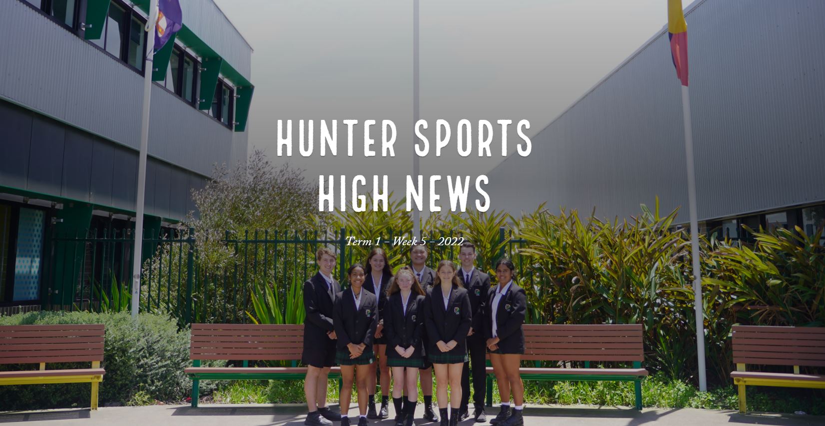 7 student leaders standing under flagpoles smiling, wearing school uniforms and blazers 